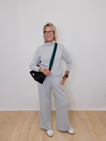 Person wearing a gray outfit with a black bag against a white wall