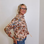 Woman wearing a floral blouse and jeans against a plain background