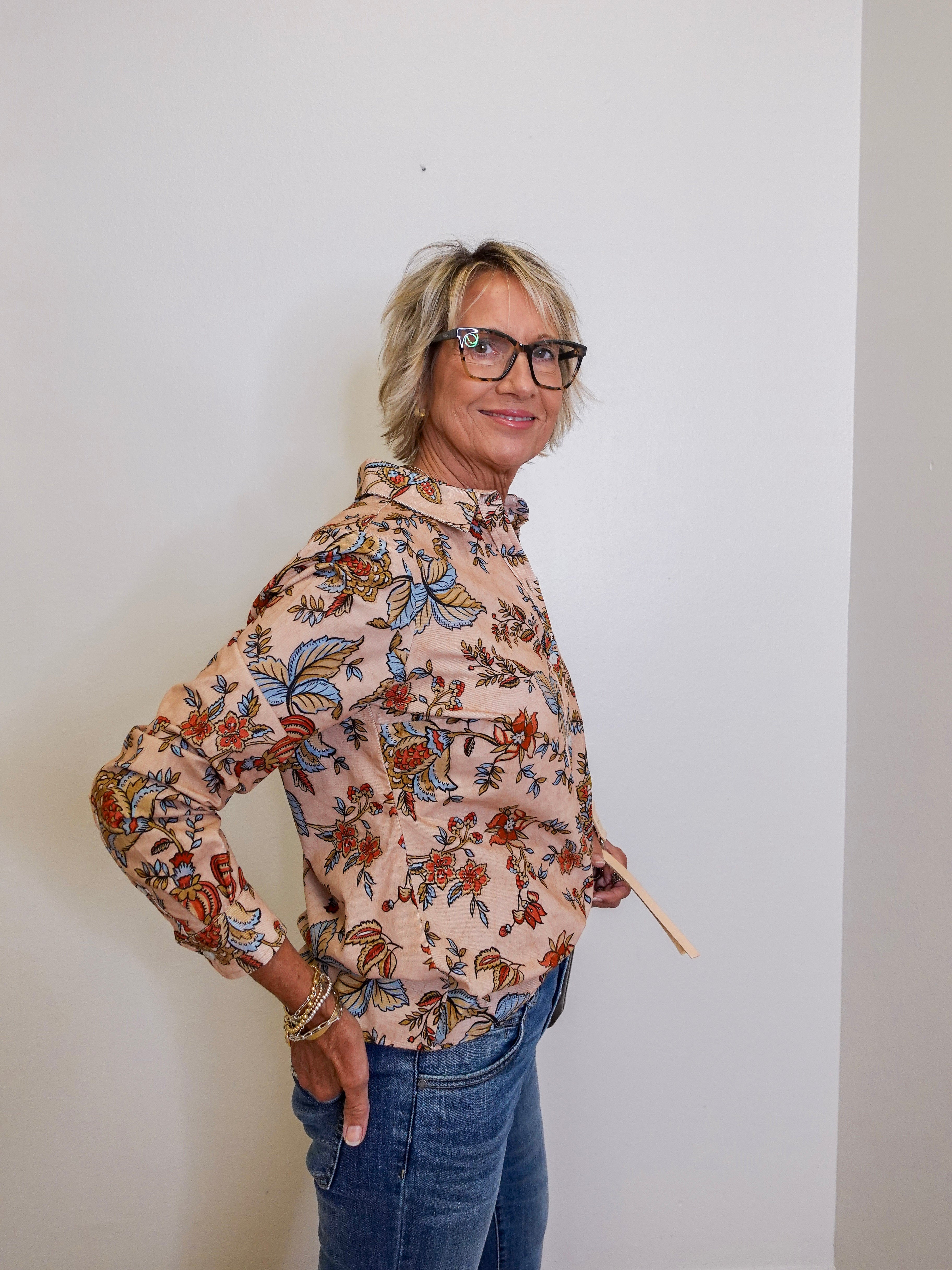 Woman wearing a floral blouse and jeans against a plain background