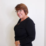 Woman wearing a black top and patterned pants against a white wall