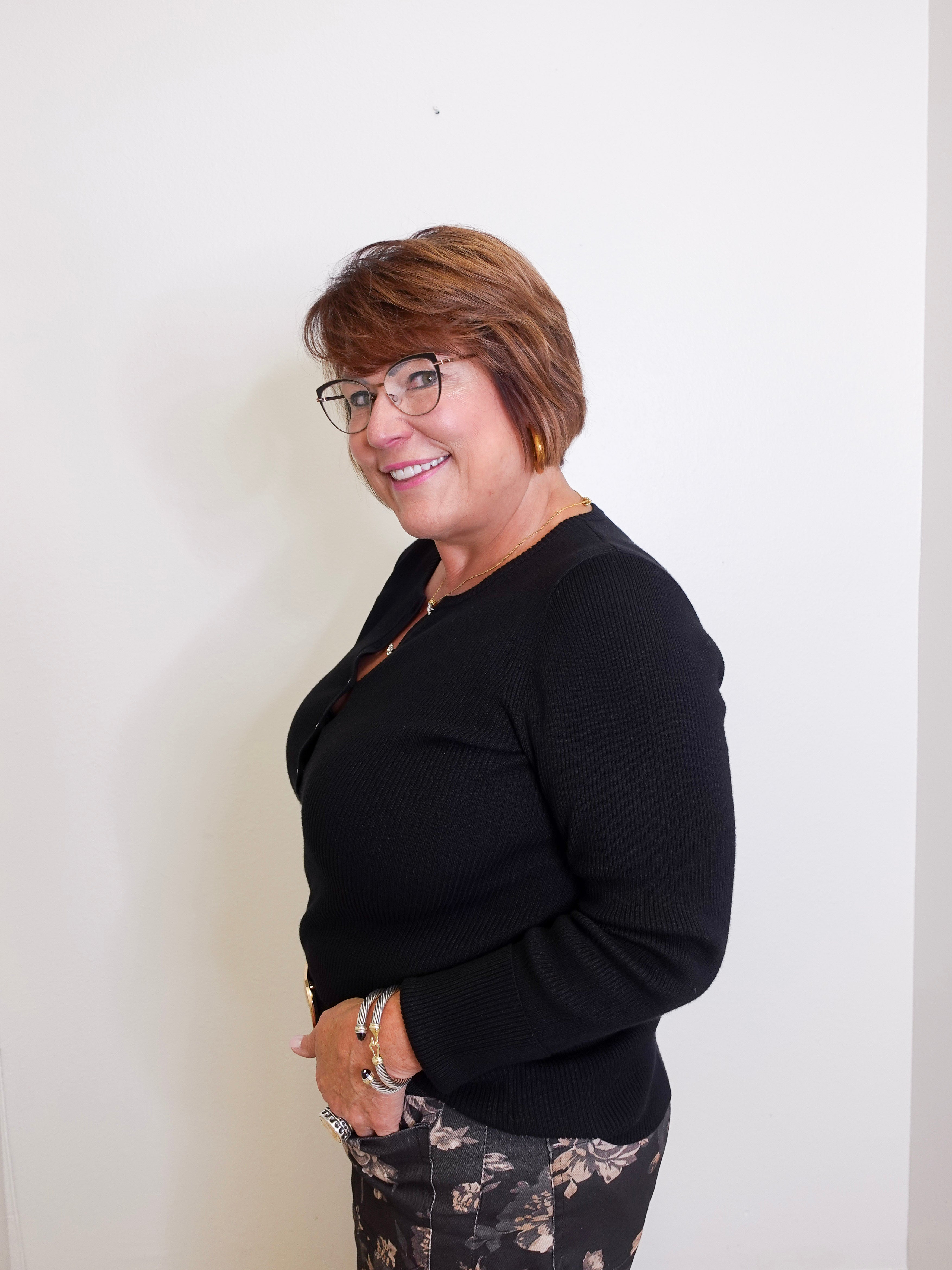 Woman wearing a black top and patterned pants against a white wall
