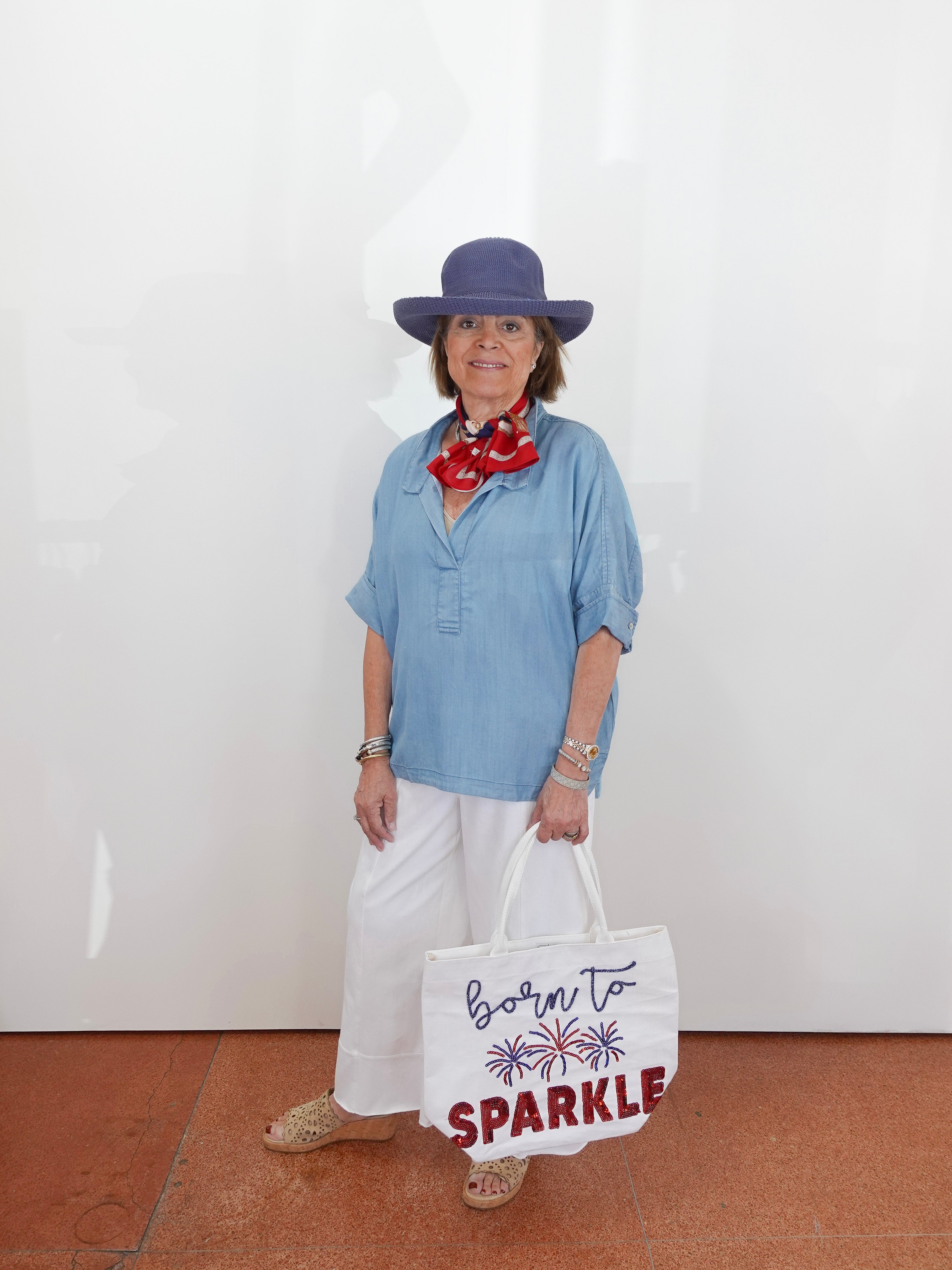 Woman wearing a blue shirt, white pants, and a purple hat, holding a tote bag with text.