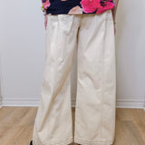 Person wearing a colorful floral top and beige wide-leg pants on a plain background