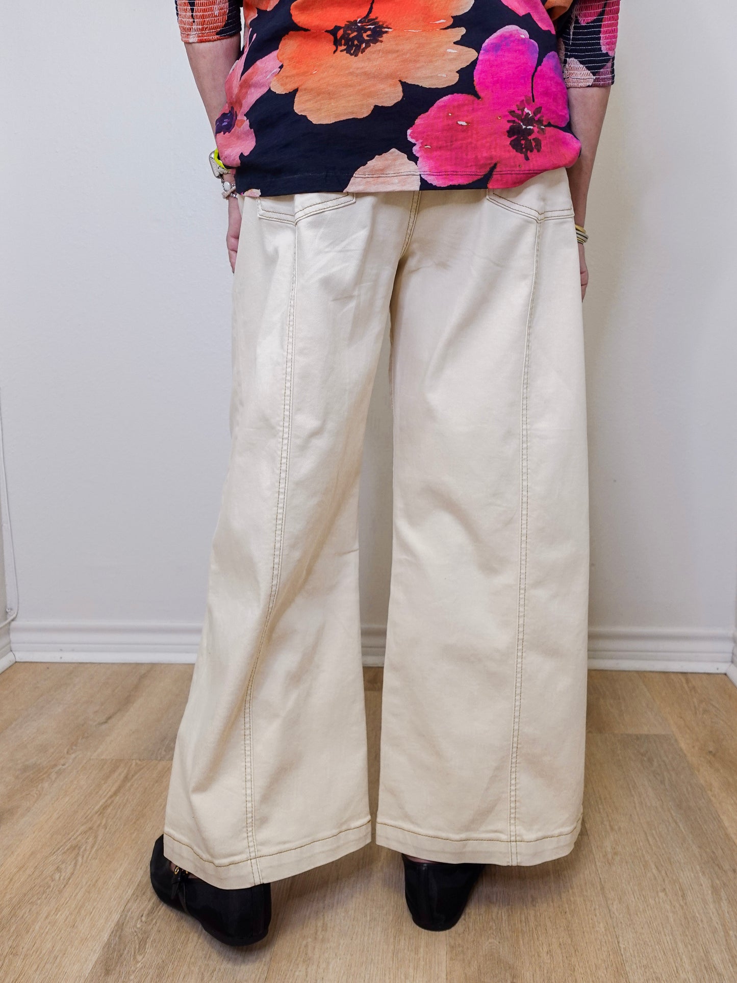 Person wearing a colorful floral top and beige wide-leg pants on a plain background