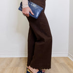 Person wearing brown wide-leg pants and blue shoes, holding a blue clutch against a white wall.