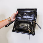 Black leather clutch bag held open by a hand against a white background