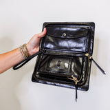 Black leather clutch bag held open by a hand against a white background