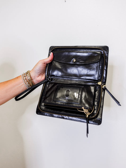 Black leather clutch bag held open by a hand against a white background