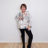 Woman wearing a patterned sweater and black knee-high boots against a white wall.