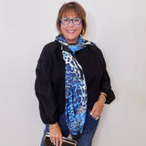 Woman wearing a black jacket, blue scarf, and glasses against a white background