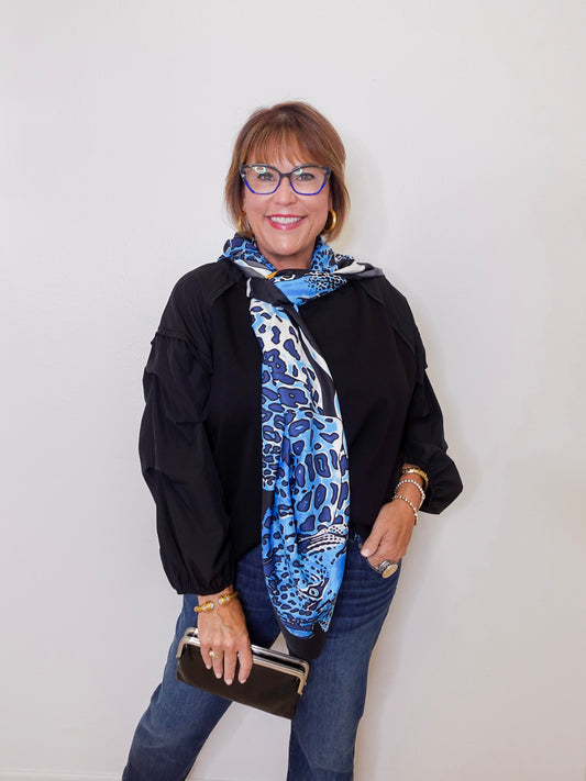 Woman wearing a black jacket, blue scarf, and glasses against a white background
