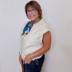 Woman wearing a white sleeveless jacket, blue jeans, and a colorful scarf against a white background