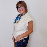Woman wearing a white sleeveless jacket, blue jeans, and a colorful scarf against a white background