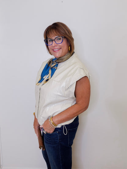 Woman wearing a white sleeveless jacket, blue jeans, and a colorful scarf against a white background