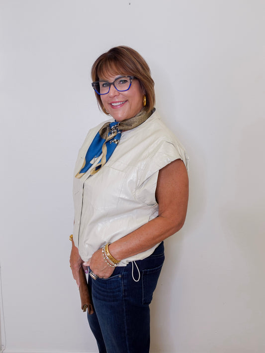 Woman wearing a white sleeveless jacket, blue jeans, and a colorful scarf against a white background