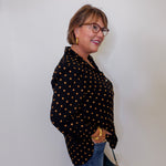 Woman wearing a black polka dot shirt and blue jeans against a white wall