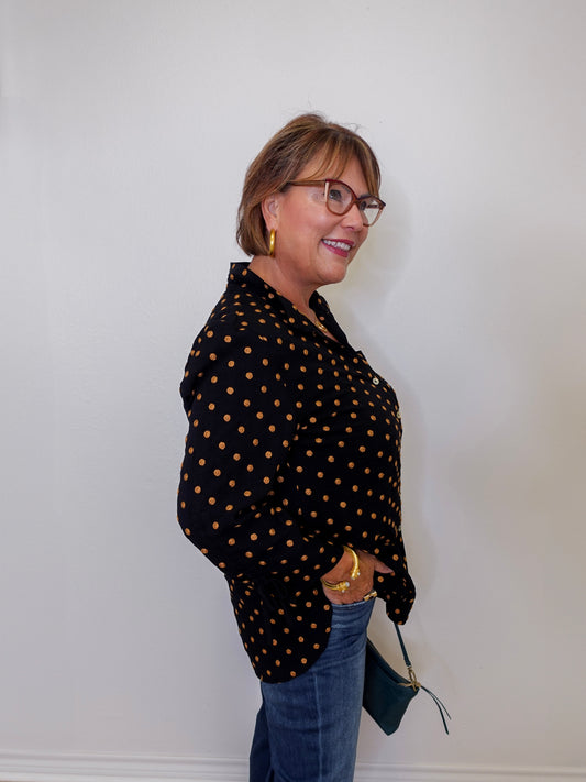 Woman wearing a black polka dot shirt and blue jeans against a white wall