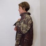 Person wearing a camouflage and leopard print jacket against a white wall