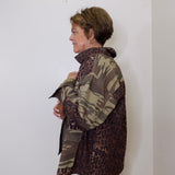 Person wearing a camouflage and leopard print jacket against a white wall