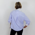 Person wearing a blue and white striped shirt with rolled-up sleeves on a plain background