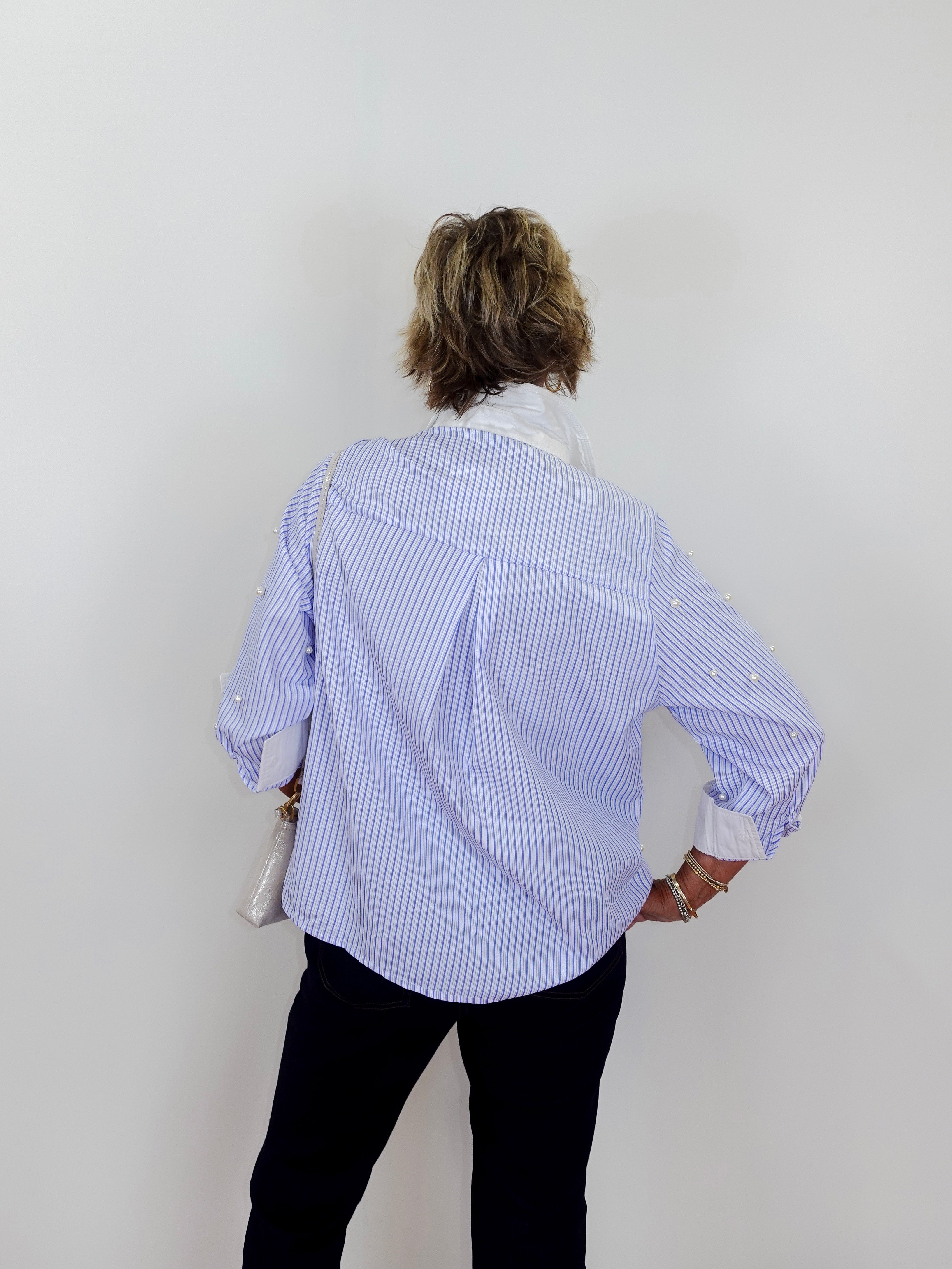Person wearing a blue and white striped shirt with rolled-up sleeves on a plain background