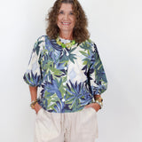 Woman wearing a colorful leaf-patterned blouse and beige shorts against a white background