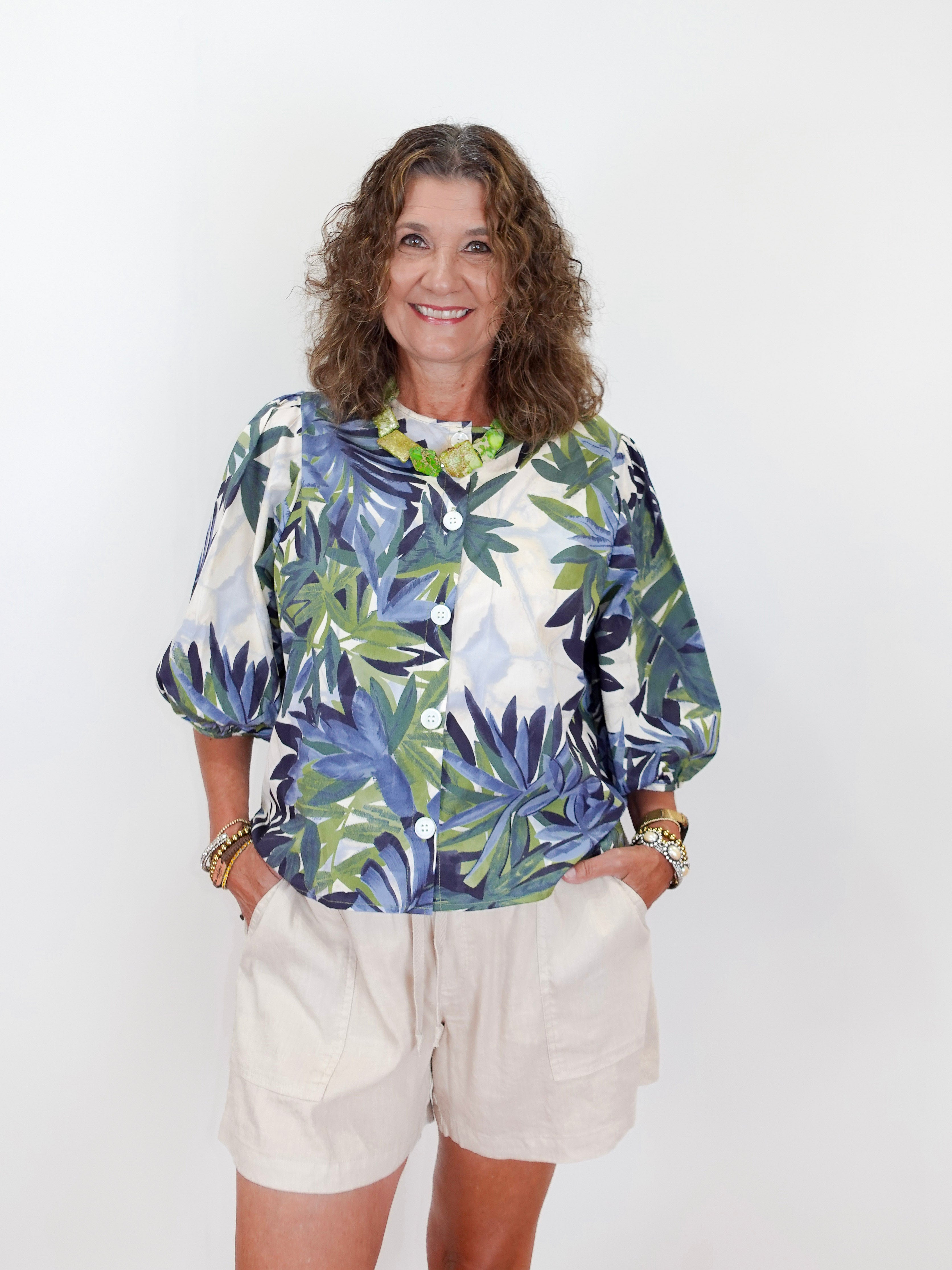 Woman wearing a colorful leaf-patterned blouse and beige shorts against a white background