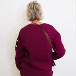 Person wearing a burgundy outfit with a brown bag against a white wall