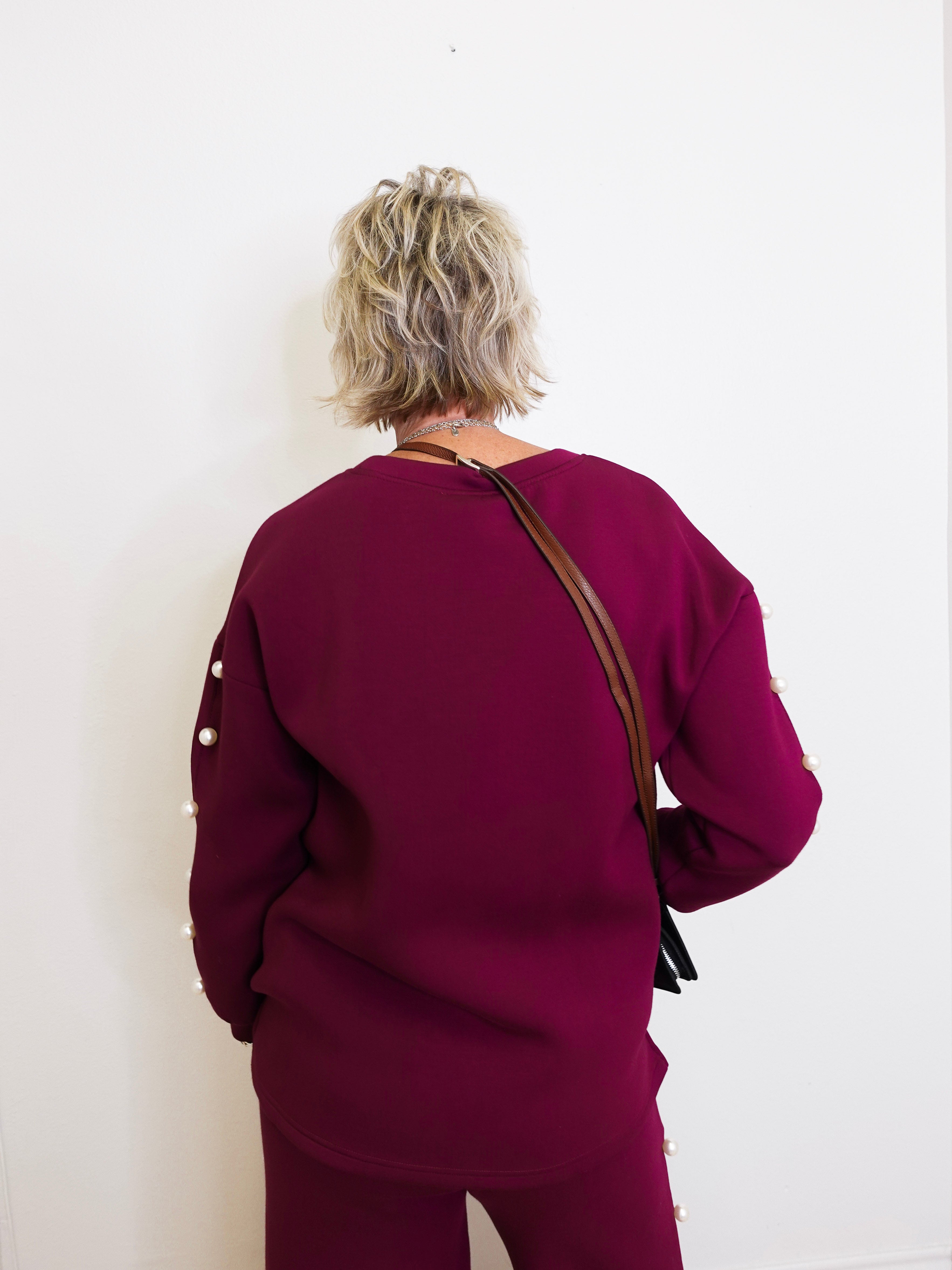 Person wearing a burgundy outfit with a brown bag against a white wall