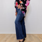 Person wearing a floral top and blue jeans standing against a white wall.