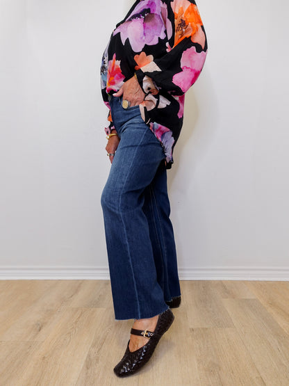 Person wearing a floral top and blue jeans standing against a white wall.