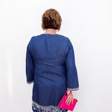 Person wearing a blue dress with white embroidery holding a pink clutch against a white background
