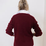 Person wearing a burgundy jacket with a white shirt underneath against a plain background