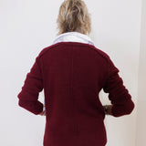 Person wearing a burgundy jacket with a white shirt underneath against a plain background