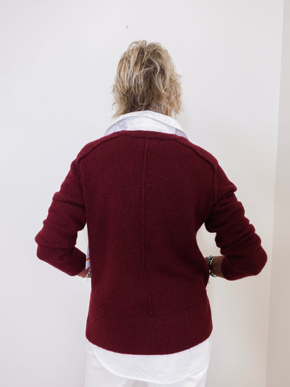 Person wearing a burgundy jacket with a white shirt underneath against a plain background