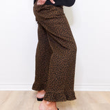 Person wearing leopard print pants and black loafers on a light wooden floor.