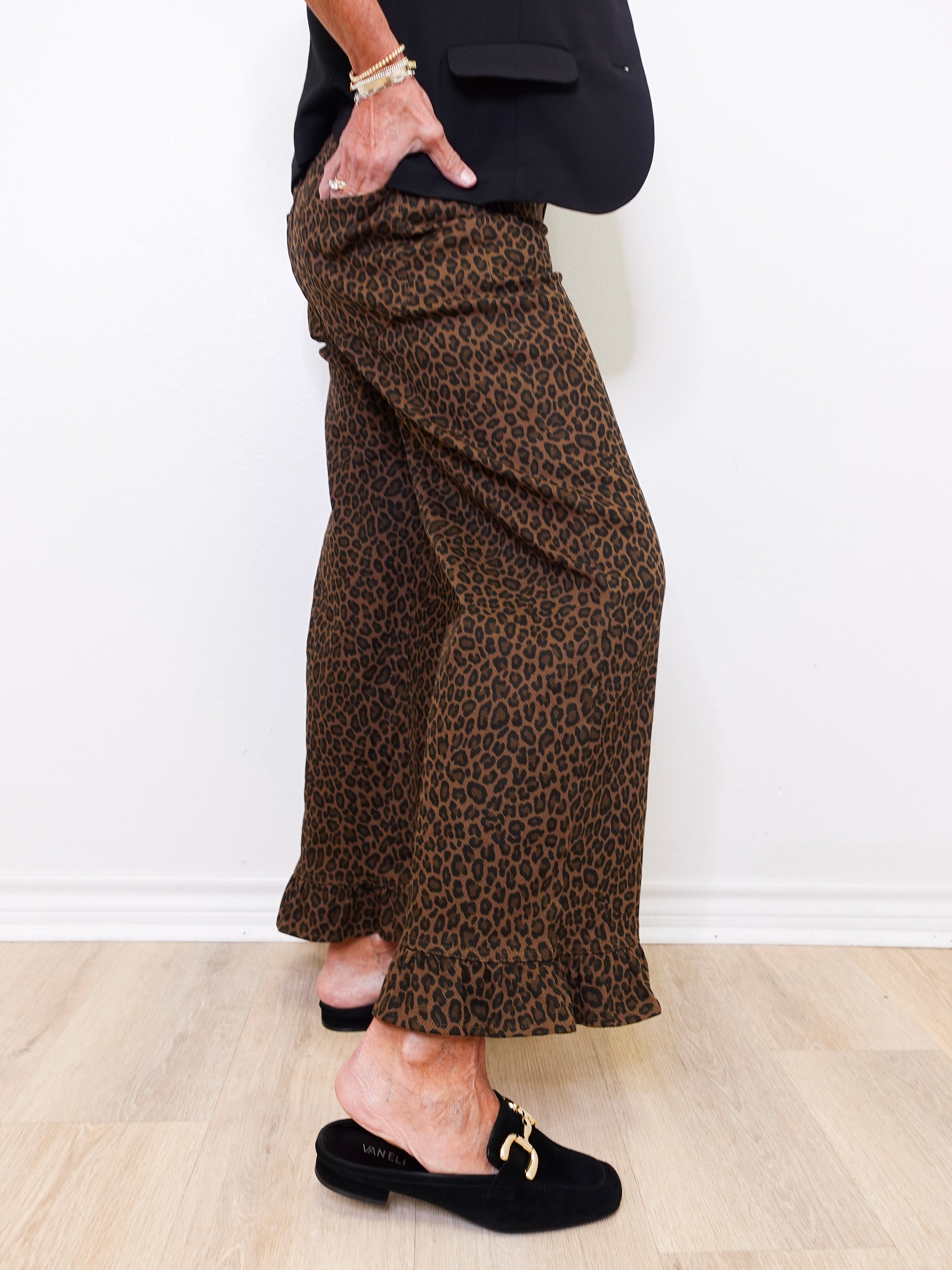 Person wearing leopard print pants and black loafers on a light wooden floor.