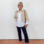 Woman wearing a beige jacket, white shirt, dark pants, and white shoes against a plain background