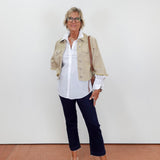Woman wearing a beige jacket, white shirt, dark pants, and white shoes against a plain background