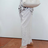 Person wearing a patterned top, white pants, and sandals, holding a white textured handbag.