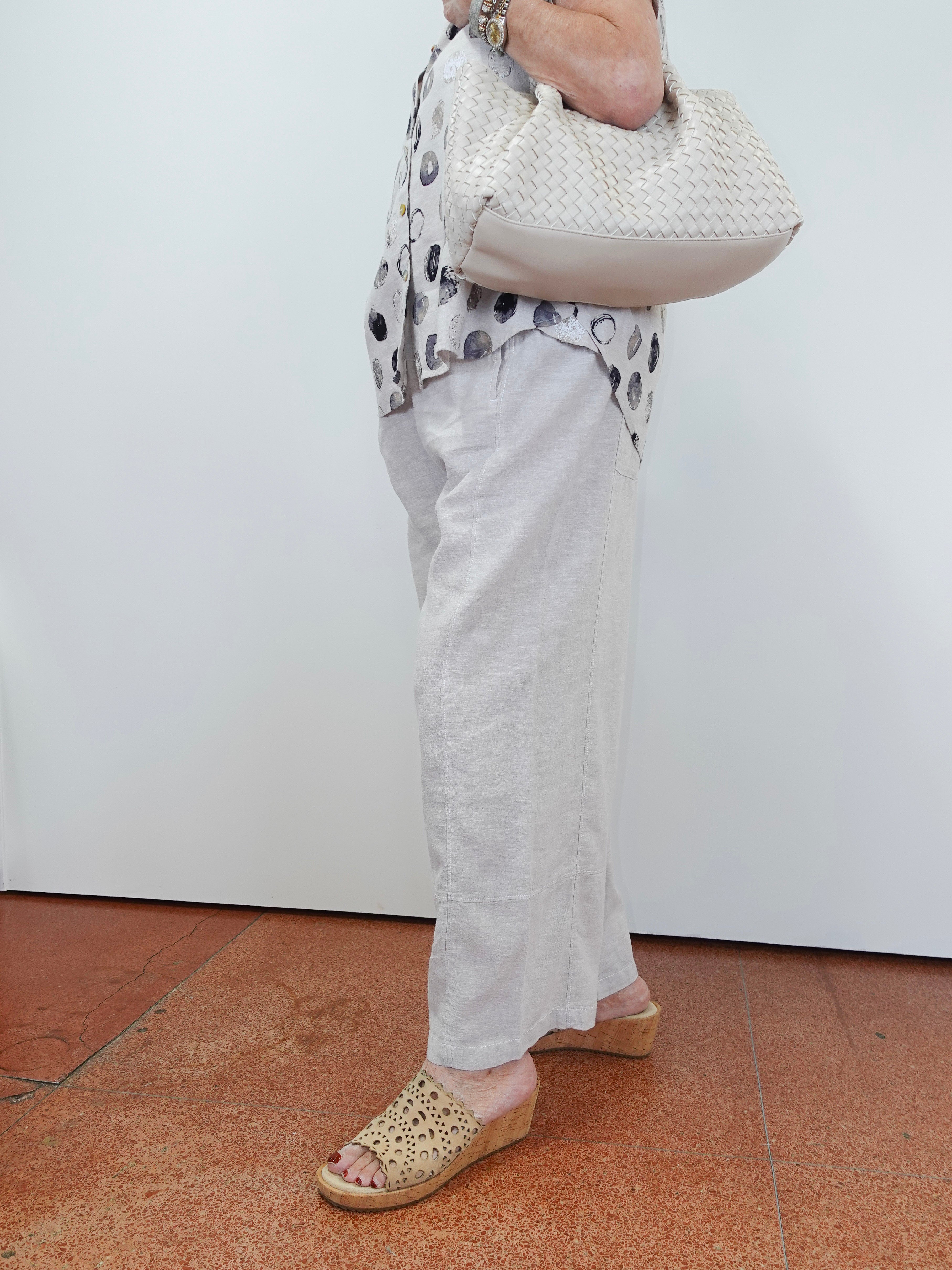Person wearing a patterned top, white pants, and sandals, holding a white textured handbag.