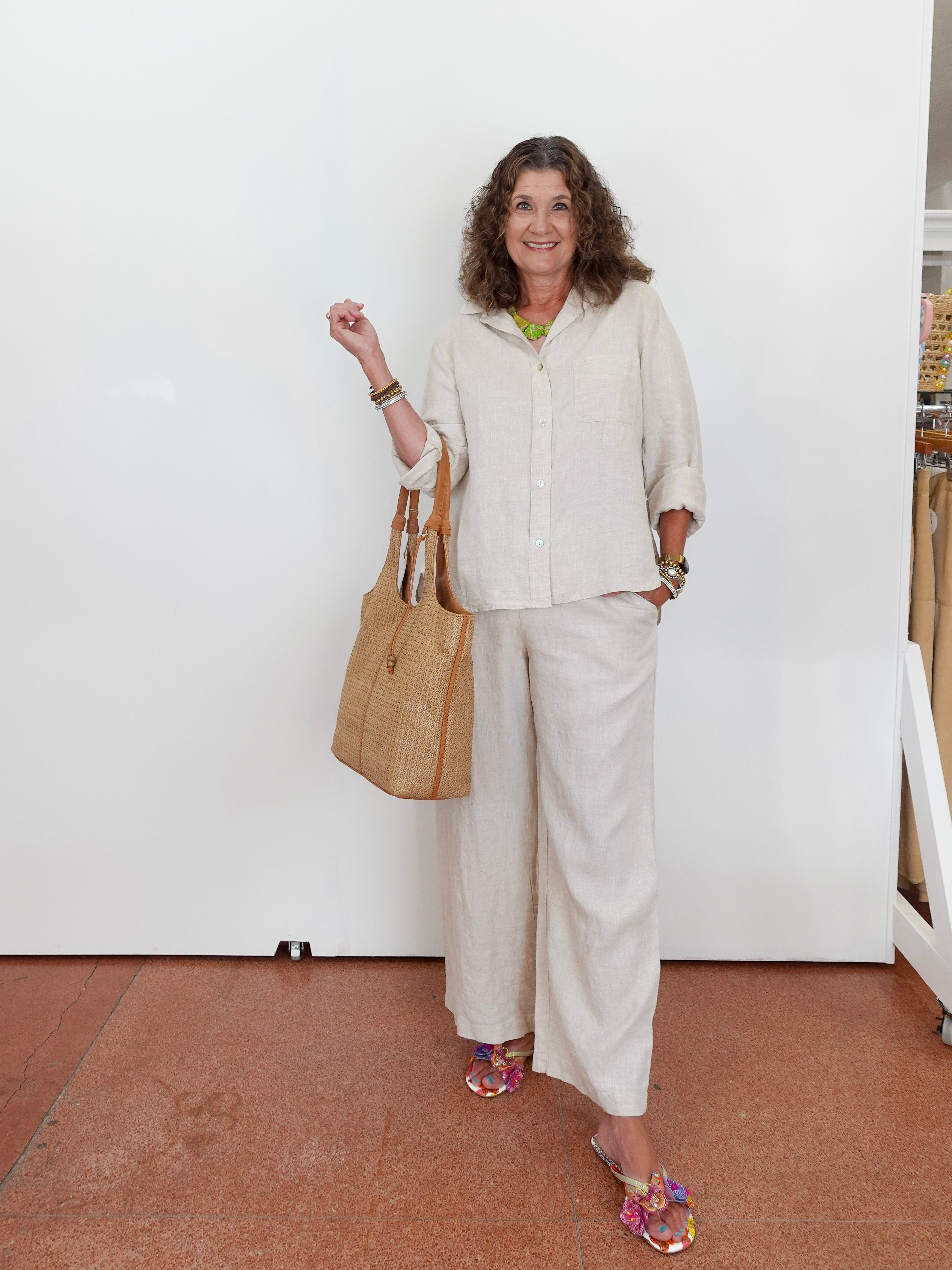 Woman in a white outfit holding a beige handbag against a white wall.
