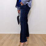 Person wearing blue jeans and a plaid jacket against a white wall.