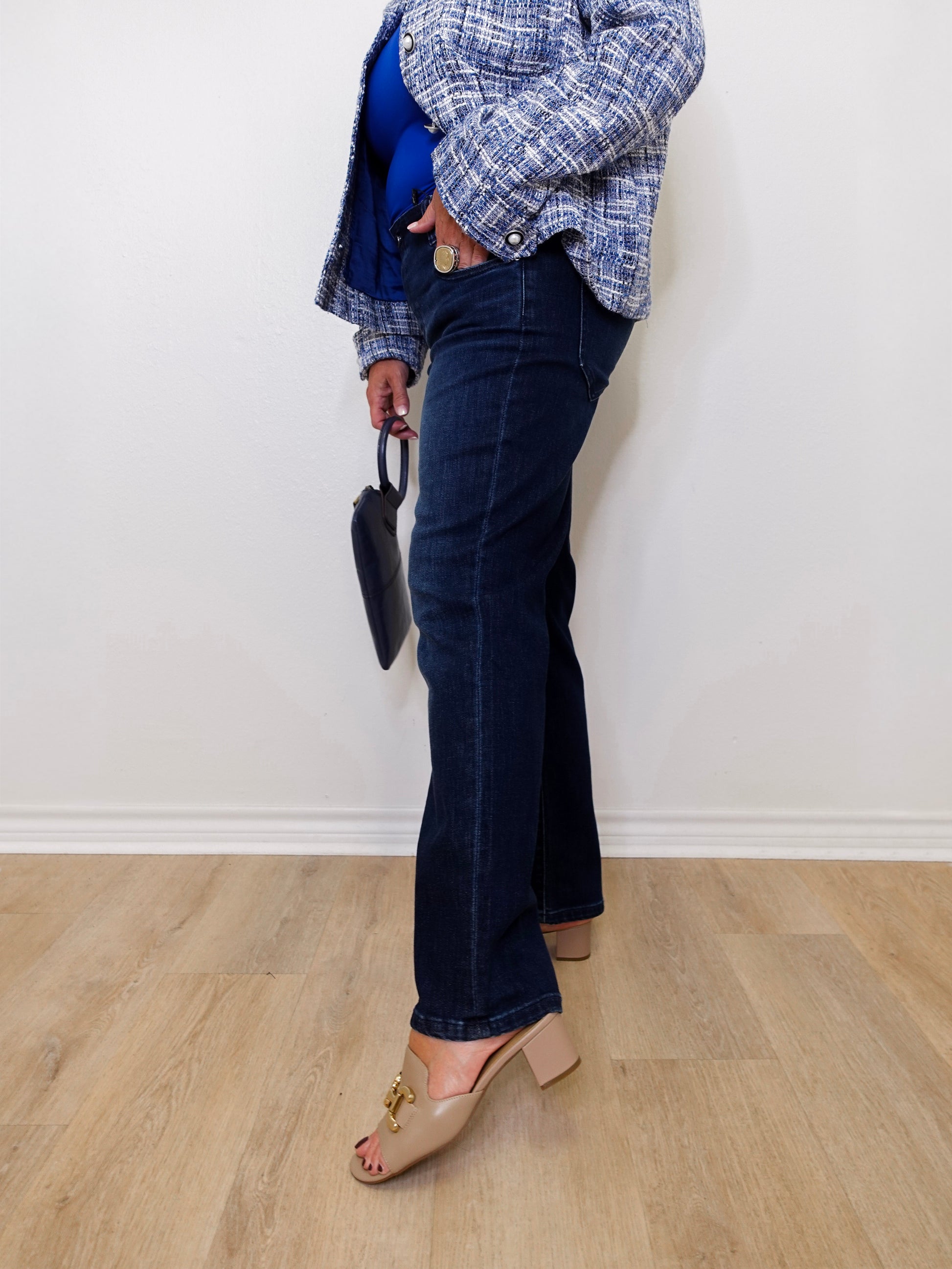 Person wearing blue jeans and a plaid jacket against a white wall.