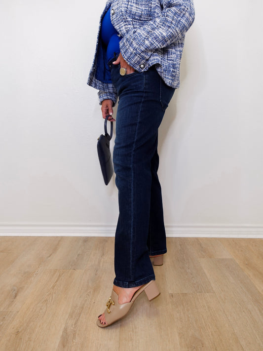 Person wearing blue jeans and a plaid jacket against a white wall.