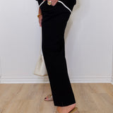 Person wearing black pants with white trim and beige sandals on a light wooden floor.