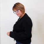 Person wearing a black sweater and blue jeans against a white wall