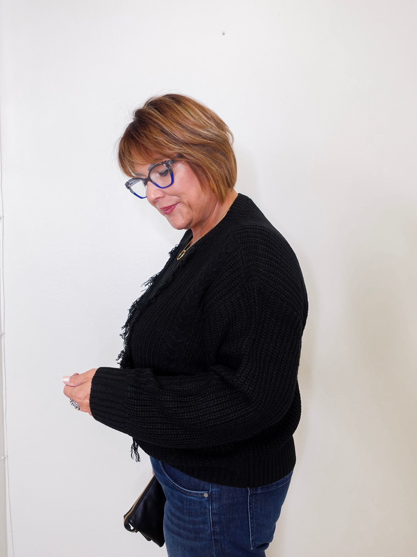 Person wearing a black sweater and blue jeans against a white wall