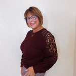 Woman wearing a burgundy sweater with lace sleeves against a white background