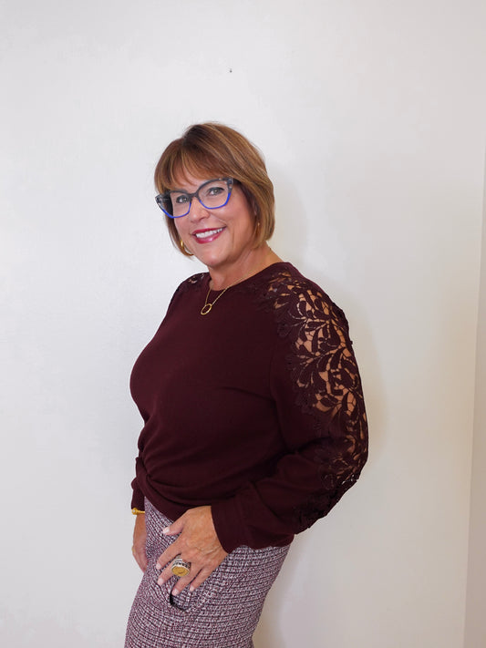 Woman wearing a burgundy sweater with lace sleeves against a white background